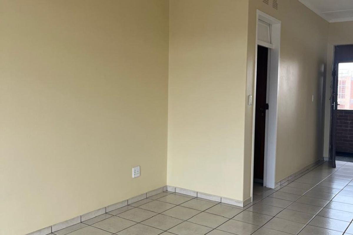 An empty living area featuring neutral wall paint, ceramic floor tiles, and a central ceiling light fixture, providing a clean and versatile space.