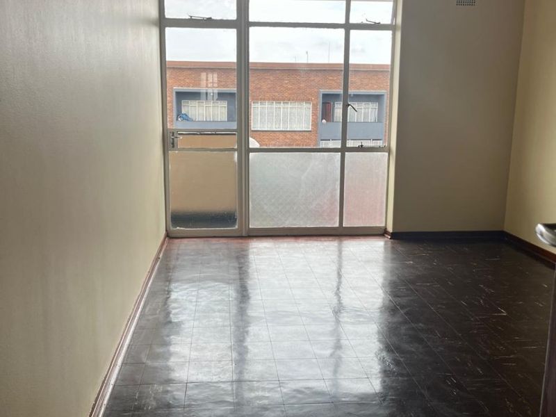 An empty living room featuring dark vinyl tile flooring, neutral walls, and a large glass door providing access to a balcony.