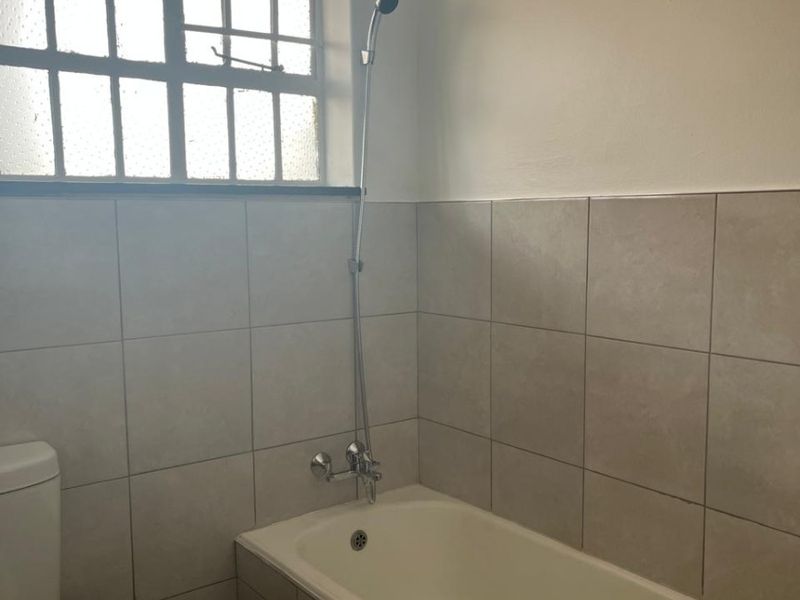 A functional bathroom featuring a bathtub with a shower mixer, tiled walls, and a toilet, providing a clean and practical space.