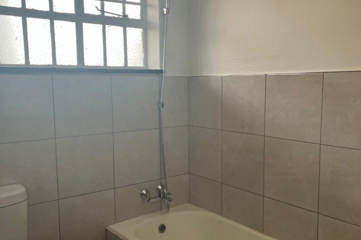 A functional bathroom featuring a bathtub with a shower mixer, tiled walls, and a toilet, providing a clean and practical space.