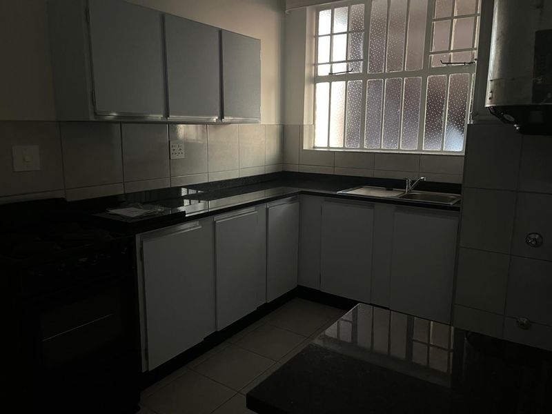 A functional kitchen featuring built-in cabinetry, granite countertops, a double sink, and tiled finishes, offering a clean canvas for potential updates.