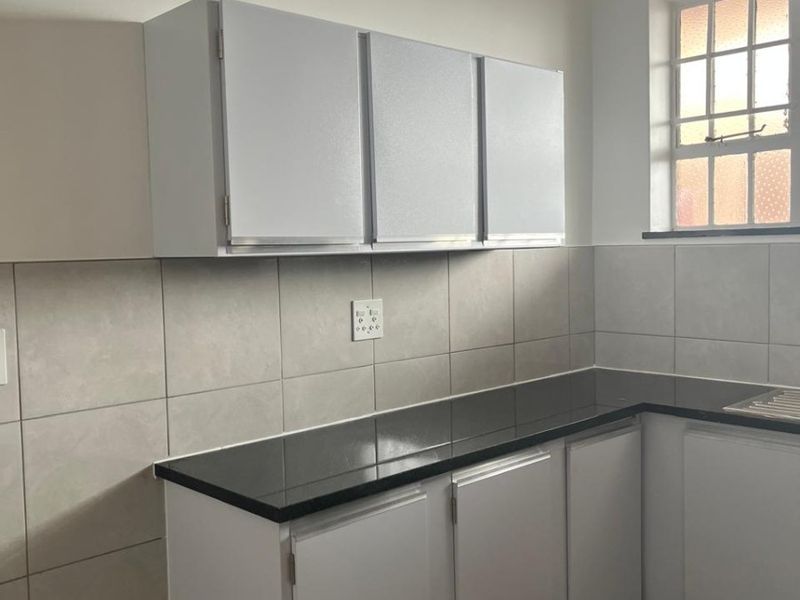 A clean, functional kitchen featuring white built-in cabinetry, dark granite countertops, and neutral tiled backsplash with a window providing natural light.