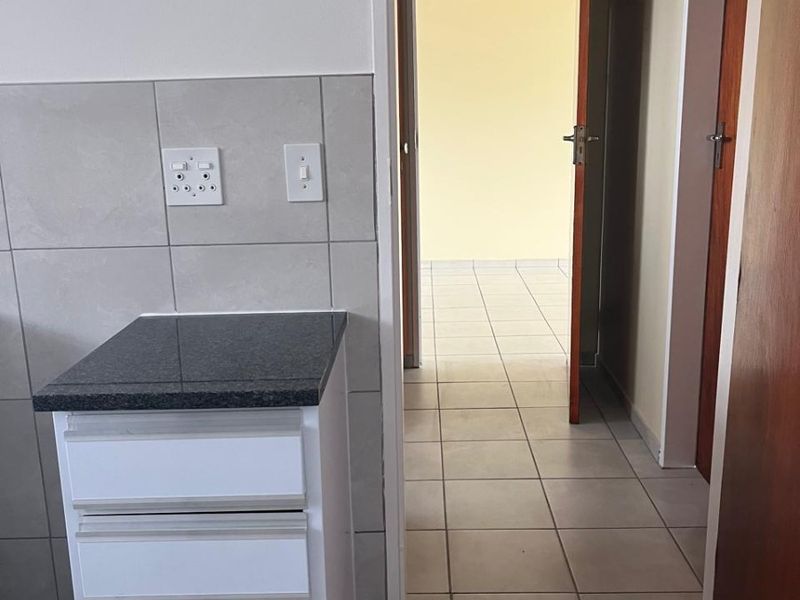 A clean kitchen area featuring modern white cabinetry, granite countertops, and neutral tiled flooring, leading into an adjacent room through a doorway.