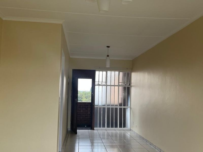 An empty, neutrally painted living area featuring tiled flooring and access to an external space through a security gate.