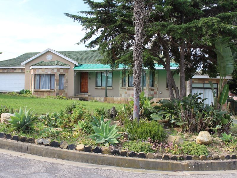 Front view of a single-story house featuring stone cladding, a green tiled roof, a covered porch, and a well-maintained landscaped front garden.