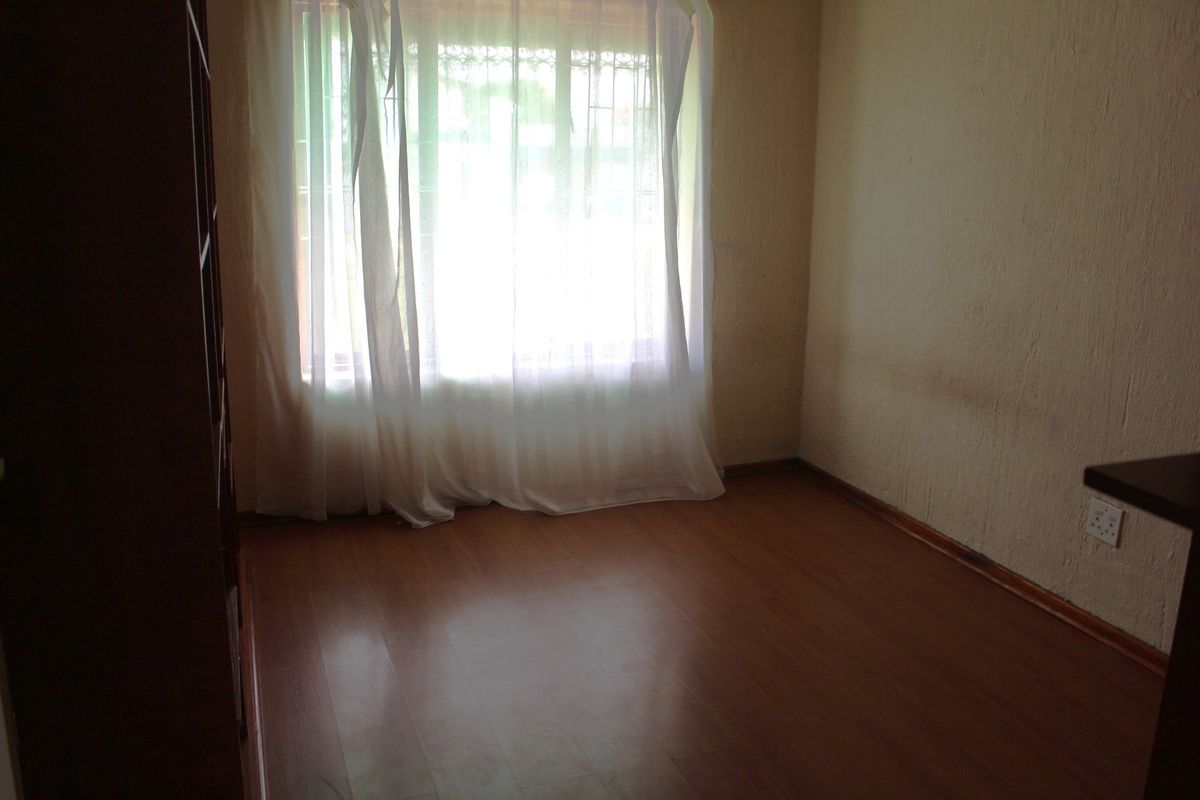 An empty bedroom featuring laminate flooring, textured walls, and a window fitted with security bars.