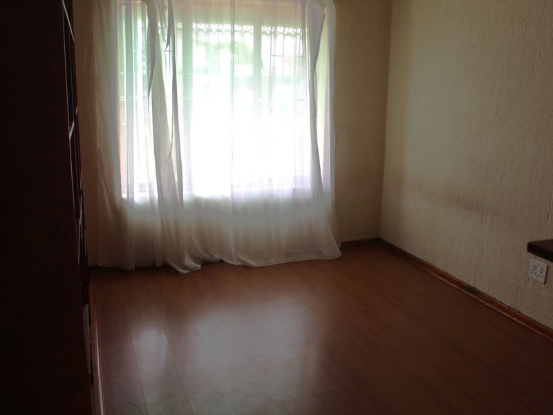 An empty bedroom featuring laminate flooring, textured walls, and a window fitted with security bars.