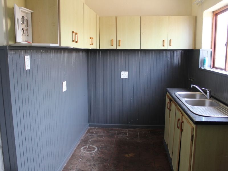 A functional scullery area featuring built-in cabinetry, a double stainless steel sink, and dark beadboard wall paneling.