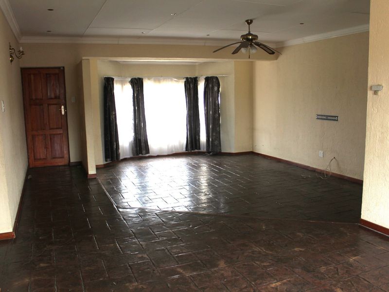 Spacious, empty living room featuring dark tiled flooring, a ceiling fan, and a large bay window providing natural light.
