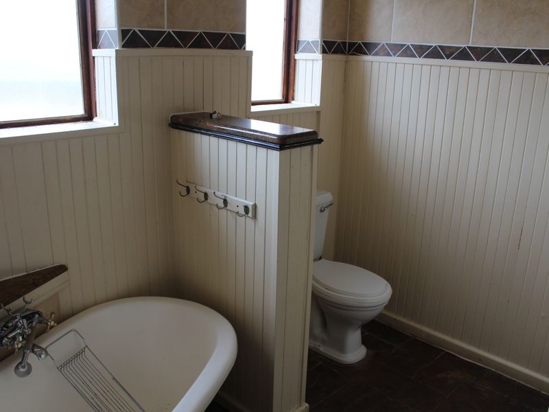 A functional bathroom featuring a freestanding bathtub, a separate toilet area, and classic beadboard wainscoting with decorative tile accents.