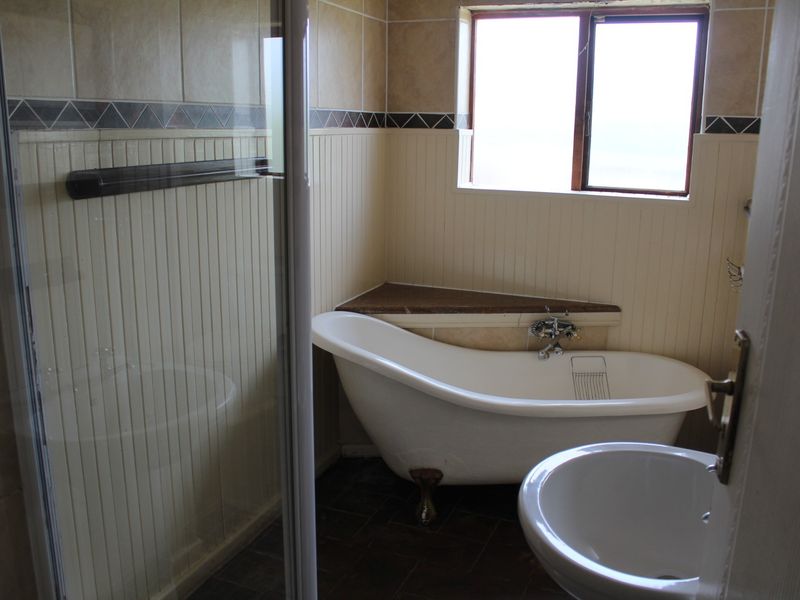A functional bathroom featuring a classic freestanding bathtub, a separate shower enclosure, and a pedestal basin with beadboard wall paneling.