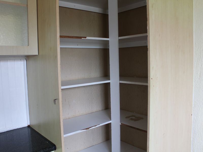A built-in pantry cupboard featuring multiple shelves, showing signs of wear and tear on the shelving edges and interior surfaces.