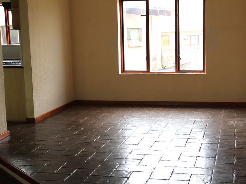 An empty living area featuring dark tiled flooring, timber window frames, and neutral wall finishes, offering a blank canvas for interior design.