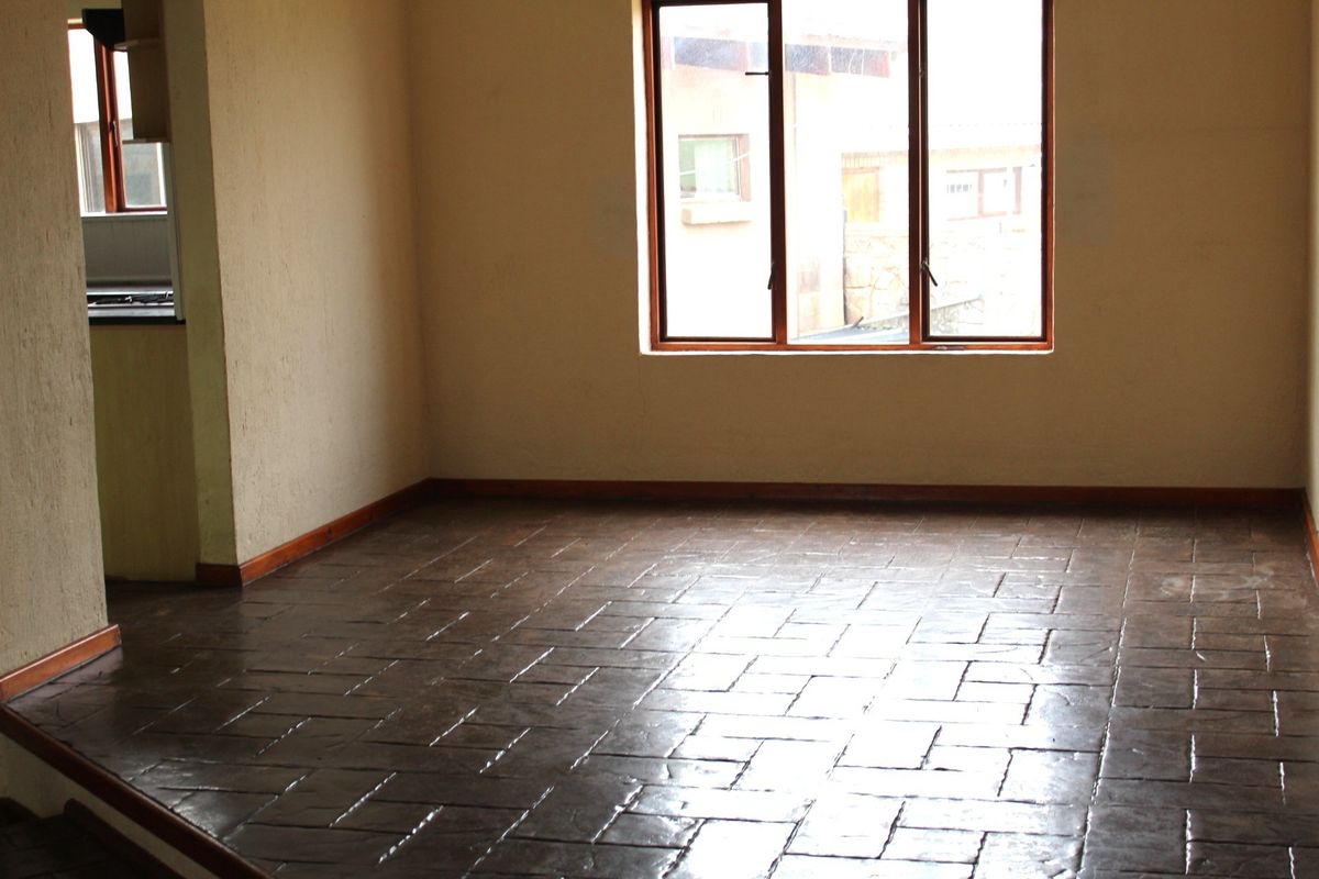An empty living area featuring dark tiled flooring, timber window frames, and neutral wall finishes, offering a blank canvas for interior design.