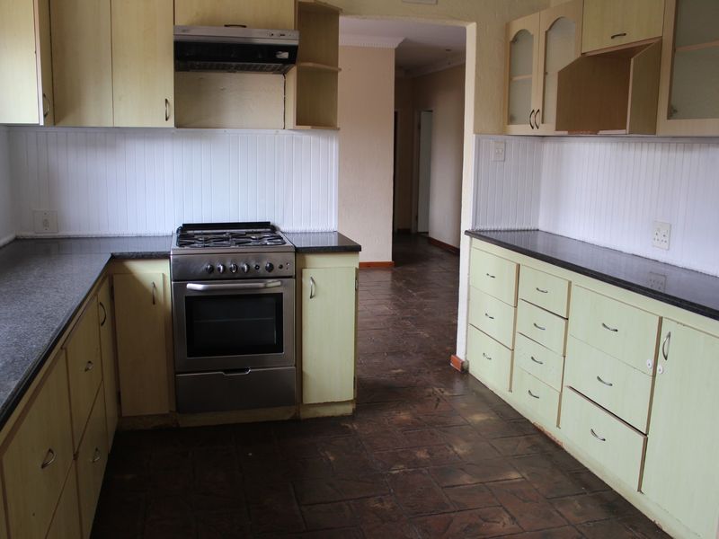 A dated kitchen featuring built-in cabinetry, a gas stove with extractor fan, and dark tiled flooring, offering significant potential for modernization.