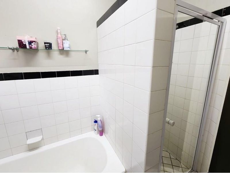 A functional bathroom featuring a built-in bathtub and a separate shower enclosure with white wall tiles and black accent detailing.