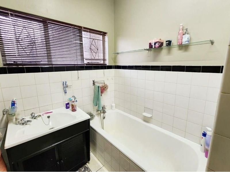 A functional bathroom featuring a bathtub, vanity basin, and tiled splashback with a wall-mounted glass shelf.