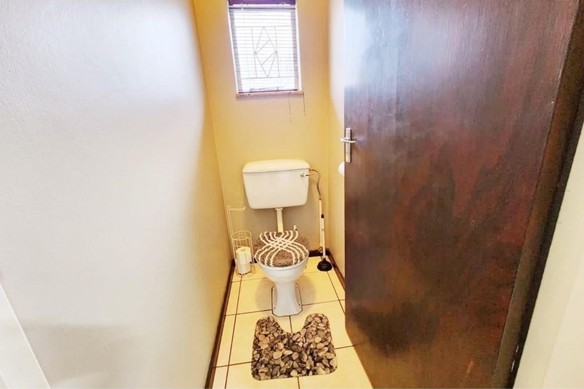 A compact guest bathroom featuring a standard toilet, tiled flooring, and a small window with fitted blinds.