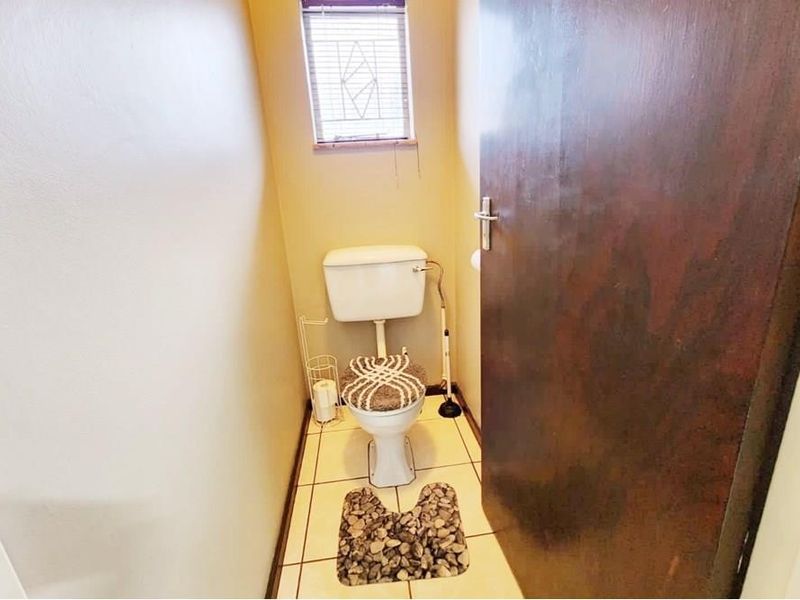 A compact guest bathroom featuring a standard toilet, tiled flooring, and a small window with fitted blinds.