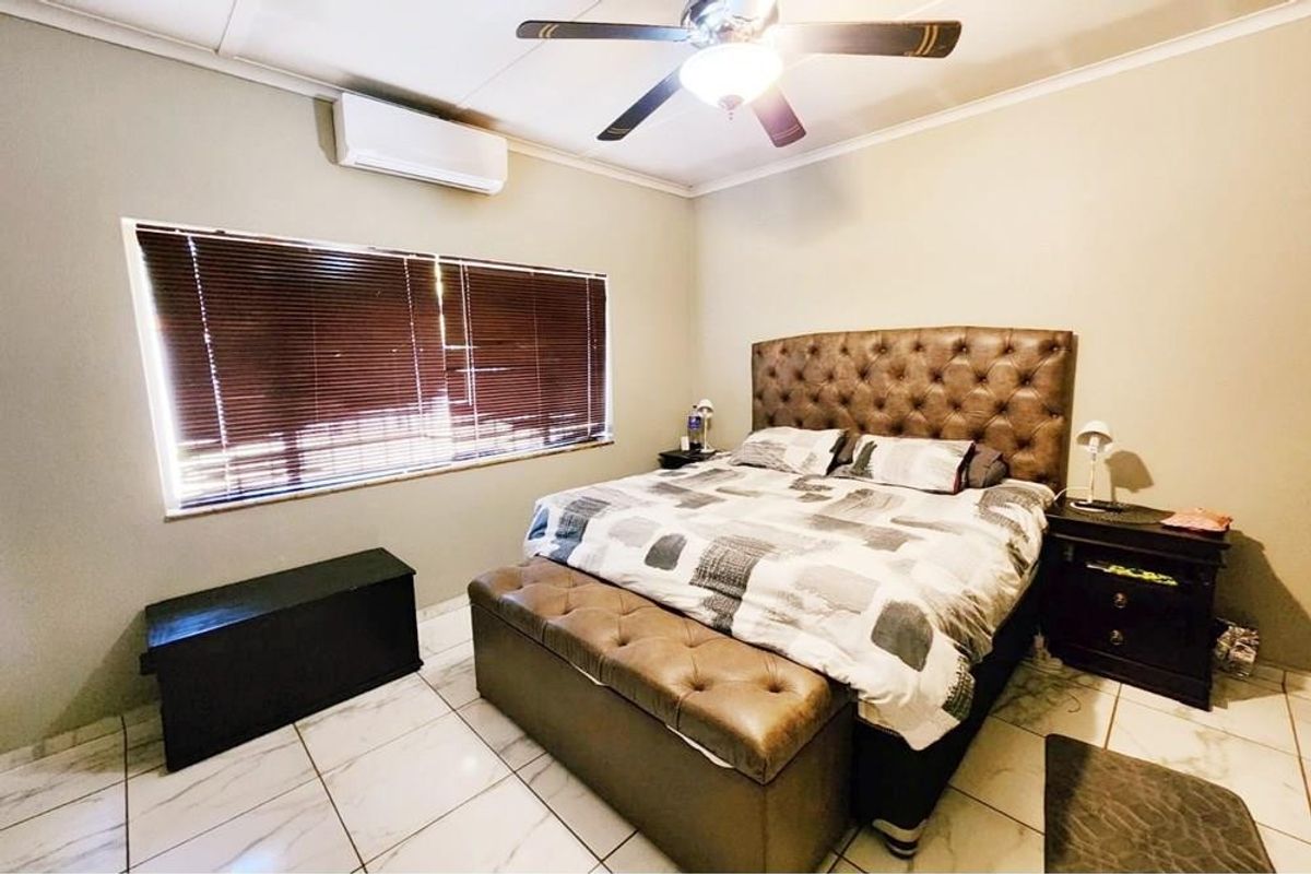 A well-maintained bedroom featuring tiled flooring, a ceiling fan, and a wall-mounted split-system air conditioner.