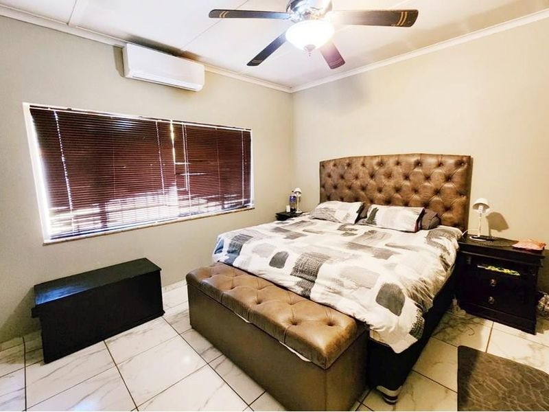 A well-maintained bedroom featuring tiled flooring, a ceiling fan, and a wall-mounted split-system air conditioner.