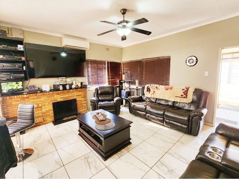 Spacious living room featuring a brick fireplace, tiled flooring, ceiling fan, and split-system air conditioning for year-round comfort.
