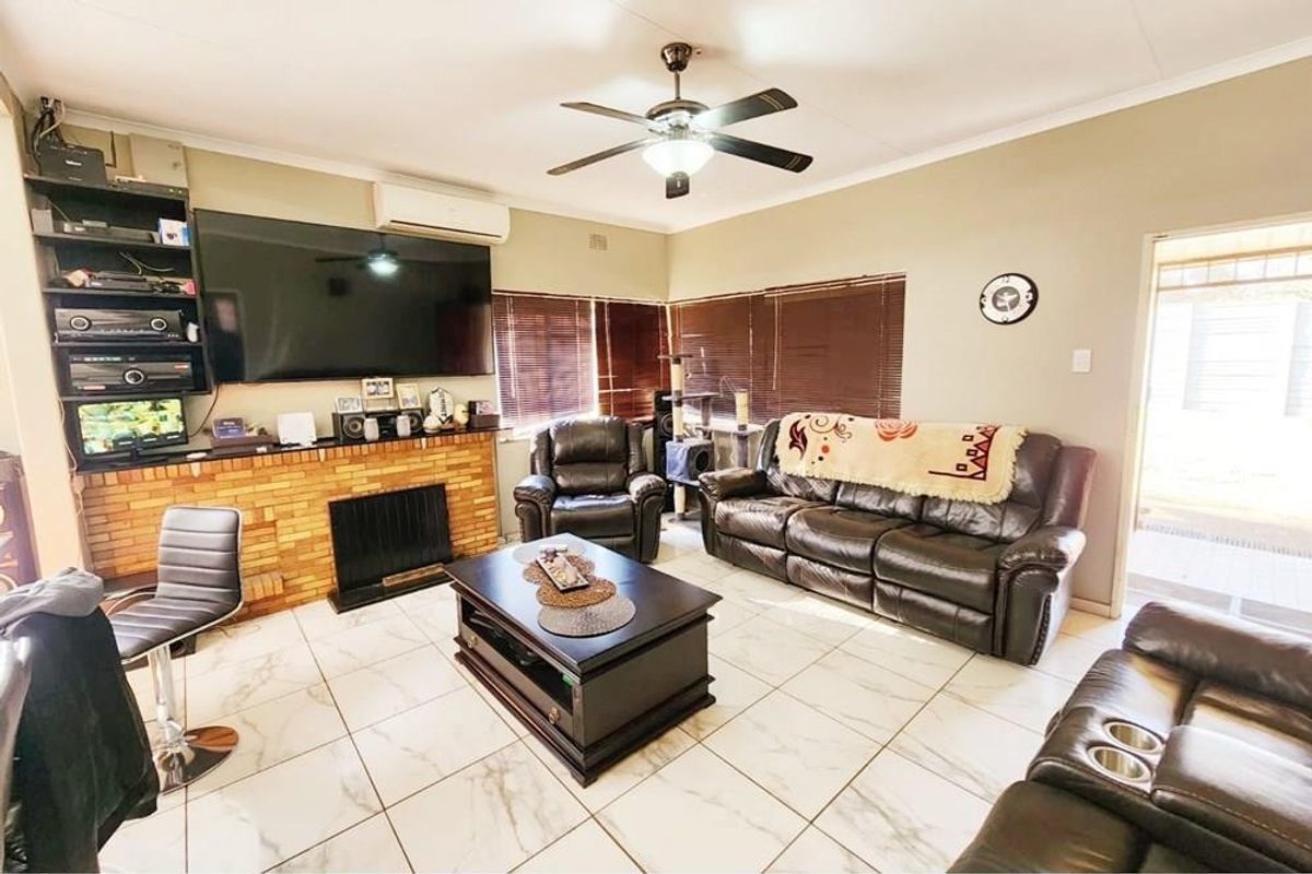 Spacious living room featuring a brick fireplace, tiled flooring, ceiling fan, and split-system air conditioning for year-round comfort.