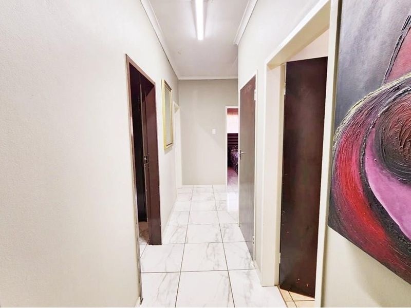 A clean, well-lit hallway featuring neutral walls, marble-look tiled flooring, and multiple internal door access points.
