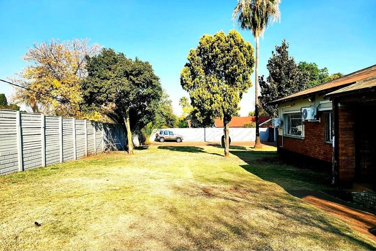 A spacious rear garden area featuring a brick exterior wall, precast concrete boundary fencing, and established trees.
