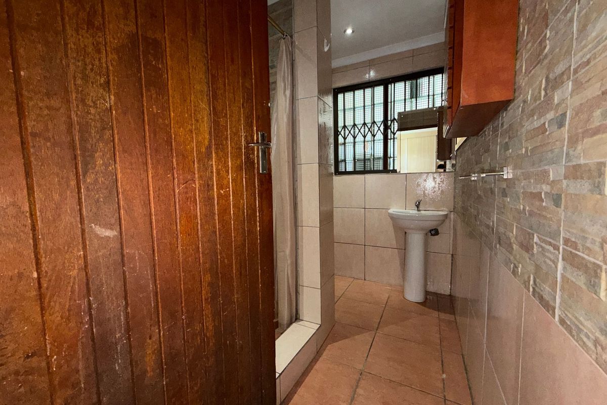 A functional bathroom featuring a pedestal basin, shower enclosure, and tiled finishes, offering a practical layout with potential for modern updates.