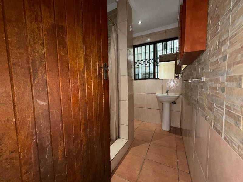 A functional bathroom featuring a pedestal basin, shower enclosure, and tiled finishes, offering a practical layout with potential for modern updates.
