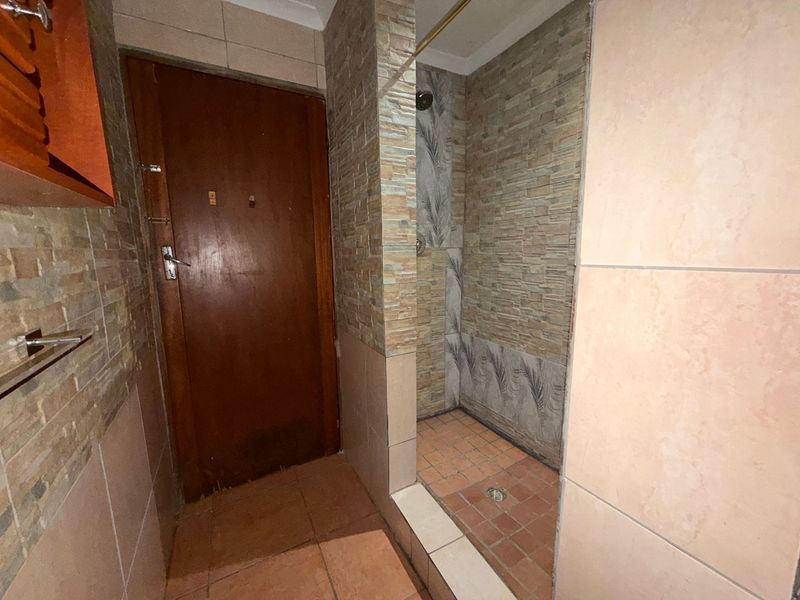 A functional bathroom featuring a walk-in shower with stone-look wall tiles and terracotta floor tiling.