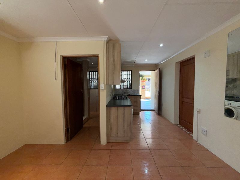 A functional kitchen area featuring built-in cabinetry, a gas hob, and tiled flooring, with direct access to an outdoor space.