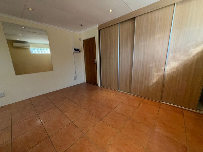 A clean, empty bedroom featuring tiled flooring, recessed lighting, a large built-in sliding wardrobe, and a wall-mounted air conditioning unit.