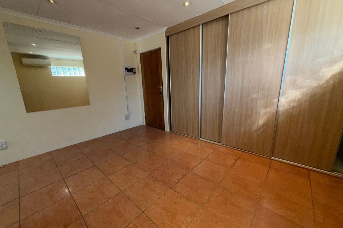 A clean, empty bedroom featuring tiled flooring, recessed lighting, a large built-in sliding wardrobe, and a wall-mounted air conditioning unit.