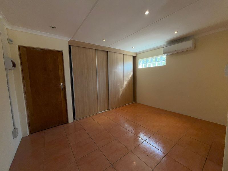 A clean, empty bedroom featuring tiled flooring, a large built-in sliding wardrobe, a split-system air conditioner, and recessed ceiling lighting.
