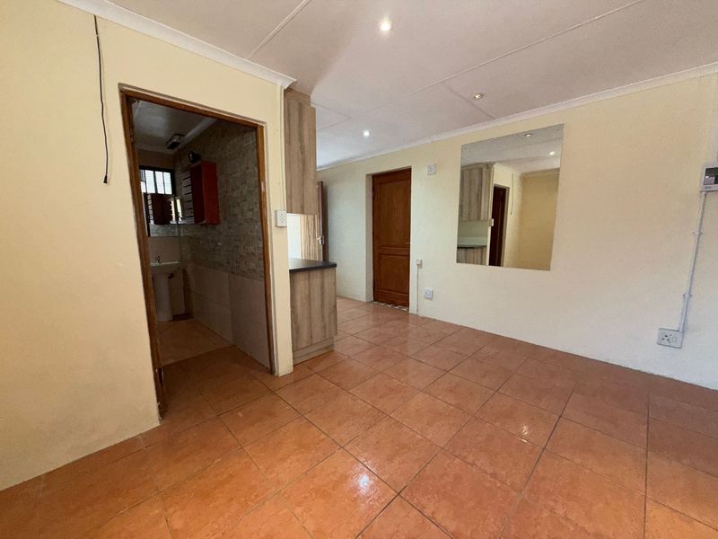 An open-plan living area featuring tiled flooring, recessed lighting, and direct access to an adjacent bathroom, presenting a blank canvas for renovation.