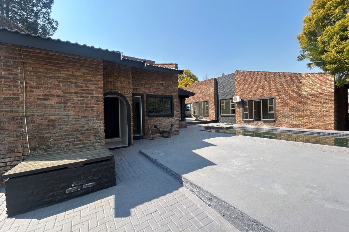 Rear exterior view featuring an exposed brick facade, a paved patio area, and a swimming pool.