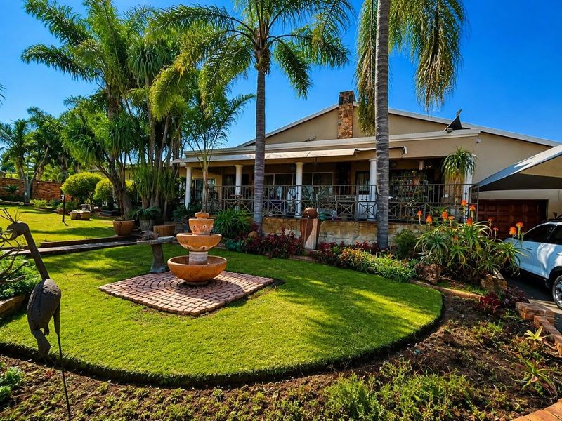 A well-maintained rear garden featuring a stone fountain, lush lawn, and a spacious covered patio with wrought iron railings and stone chimney detail.
