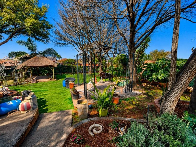 A spacious garden featuring a metal gazebo, a traditional thatched lapa, and established trees, offering a versatile outdoor entertainment space.