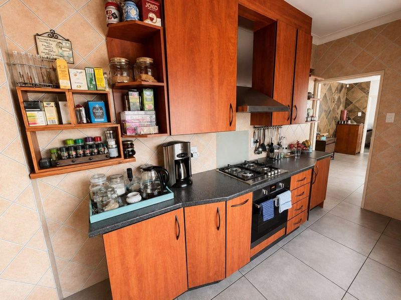 A functional kitchen featuring wooden cabinetry, a gas hob with extractor fan, built-in oven, and tiled finishes throughout.