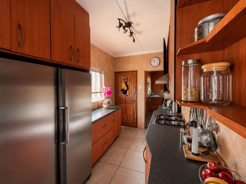 A functional kitchen featuring wood-finish cabinetry, dark countertops, a gas hob, and tiled finishes, with a view through to an adjacent scullery area.