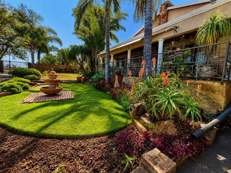 A well-maintained rear garden featuring a stone fountain, lush landscaping, and a covered patio with stone cladding and wrought iron railings.