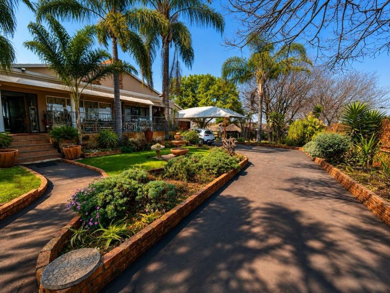 A well-maintained front exterior featuring a paved driveway, landscaped garden beds with brick edging, stone steps leading to a covered patio, and a carport.