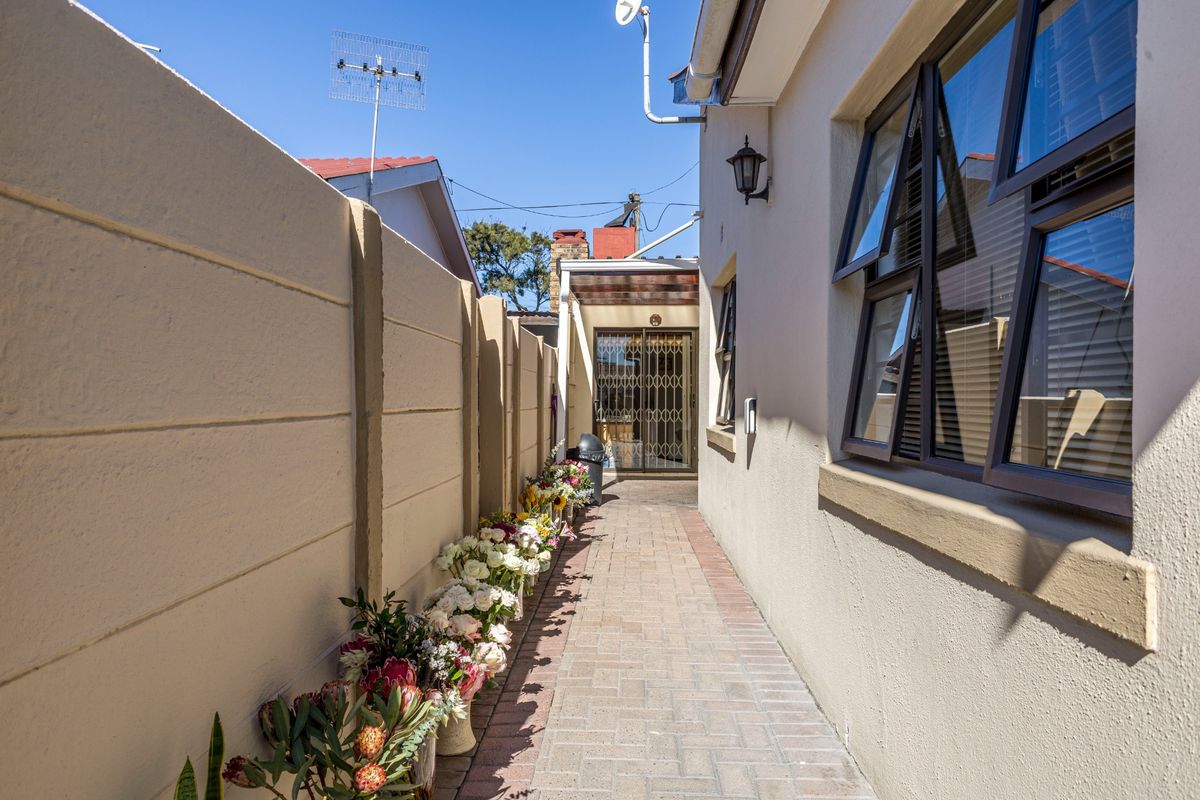 A narrow paved side walkway leading to the rear of the property, featuring a secure boundary wall and aluminium window frames.