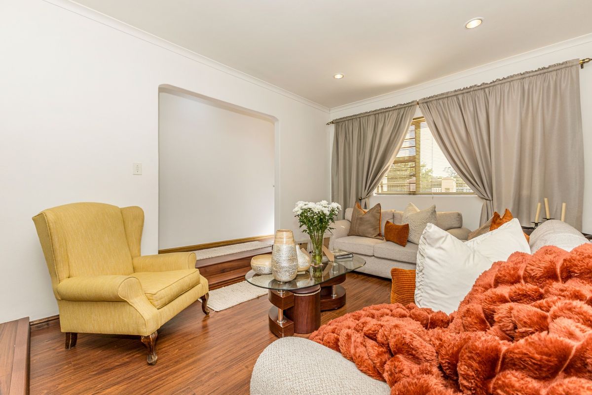 A comfortable living room featuring laminate flooring, recessed downlights, and an arched transition to an adjacent space, complemented by natural light from the window.