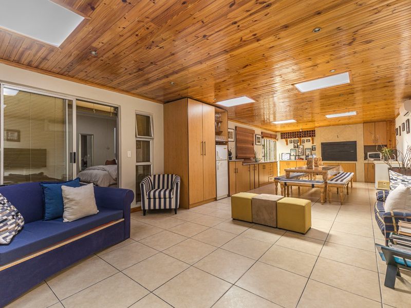 Spacious open-plan living and kitchen area featuring a timber-clad ceiling with skylights, tiled flooring, and direct access to an adjacent bedroom via sliding doors.