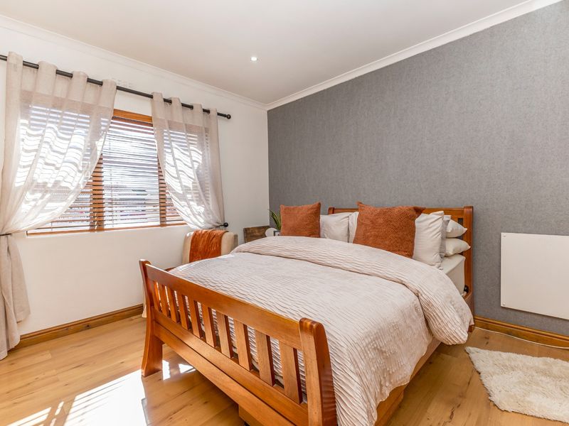 A well-maintained bedroom featuring timber flooring, a grey feature wall, and a wall-mounted heater, offering a clean and comfortable living space.