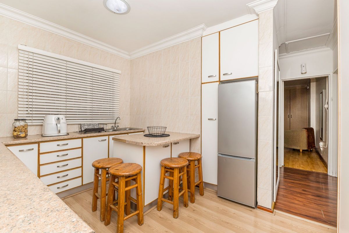 A functional kitchen featuring built-in cabinetry, laminate countertops, and a stainless steel sink, with neutral wall tiling and crown molding details.