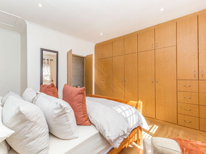 A well-maintained bedroom featuring extensive built-in wooden cabinetry, laminate flooring, recessed lighting, and convenient access to an en-suite bathroom.